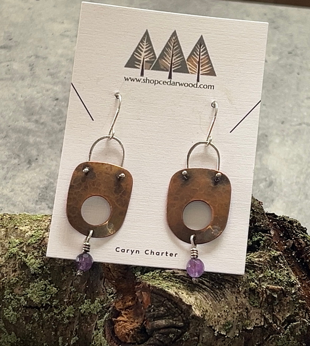 Retangular hammer brass dangle earring with a whole in the lower half of the body. An amethyst bead hangs off the bottome. Sterling silver wire trim and earwires provide a contrasting accent with the brass.